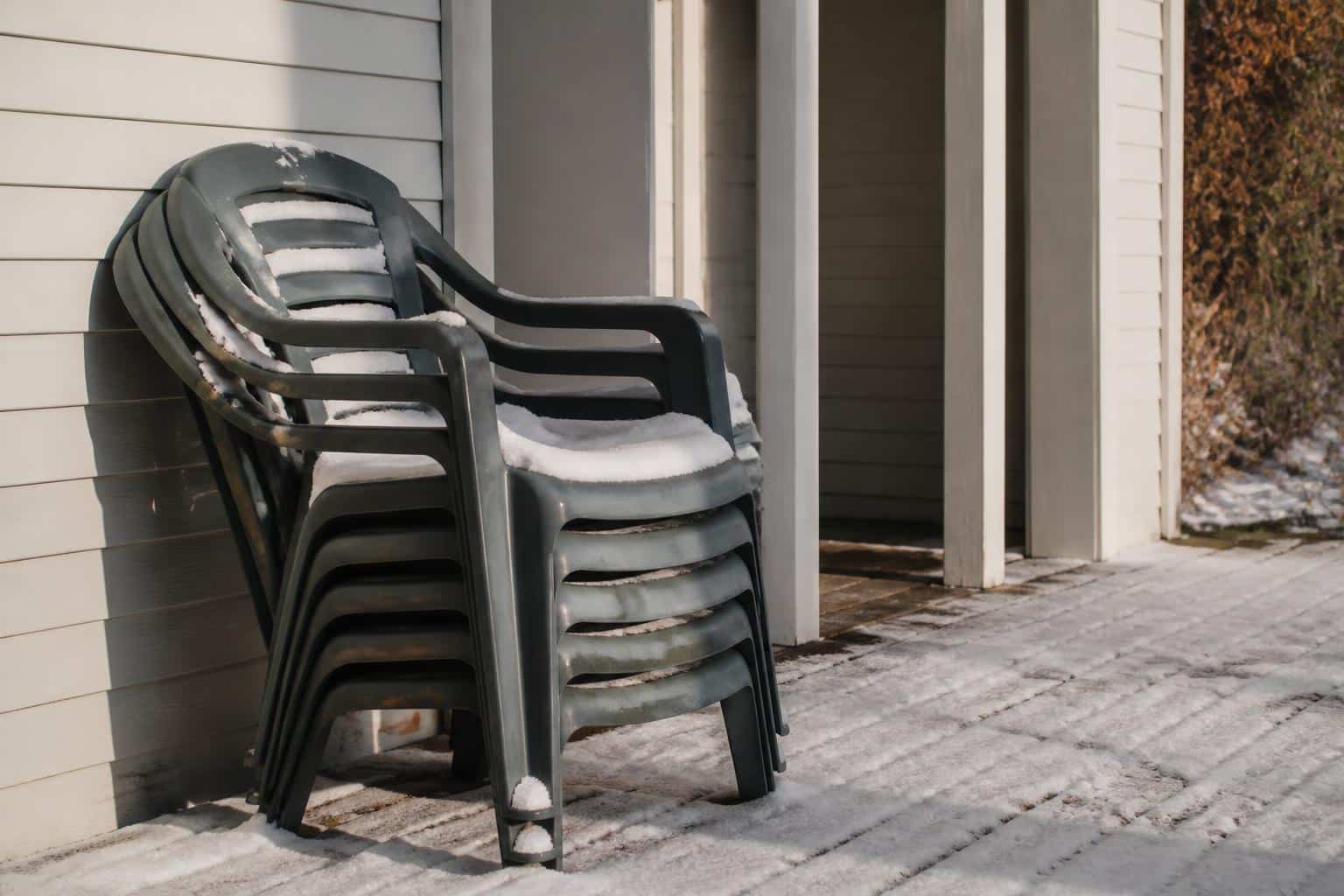 Stacked plastic patio chairs dusted with light snow beside a covered porch