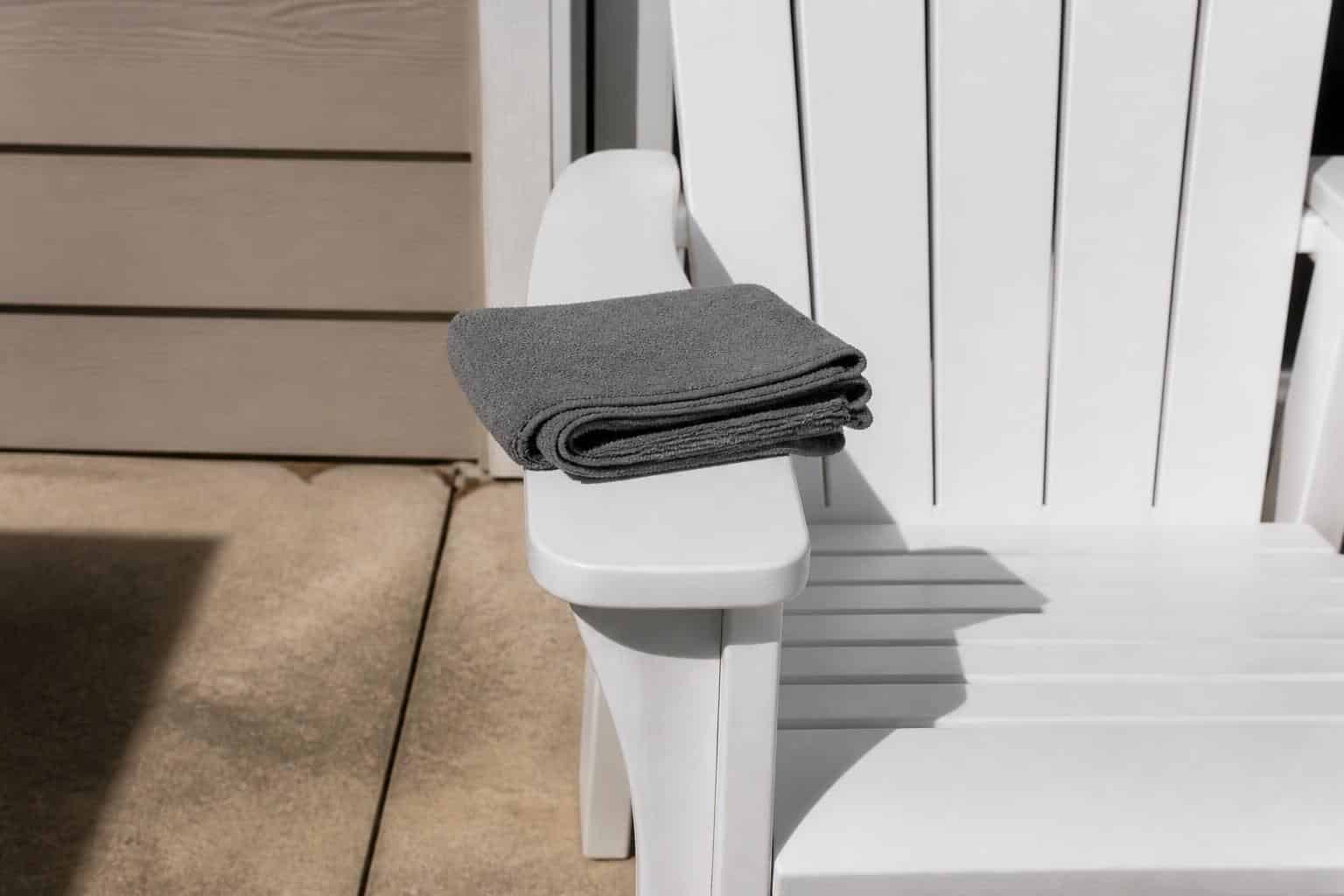 Close-up of a spotless white plastic patio chair seat with a folded microfiber cloth resting on the armrest
